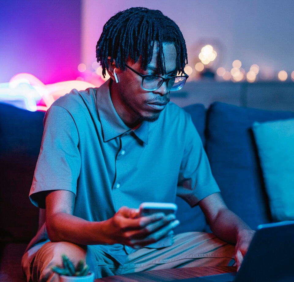 Head Banner describing a man sitting at his home checking his phone and notebook at the same time.